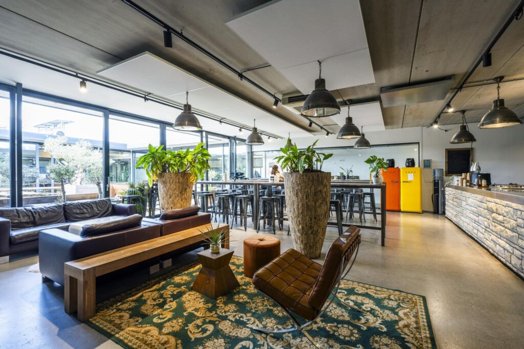 Modern communal lounge and kitchen area on Johan van Hasseltweg with industrial design, large plants, leather seating, and colorful retro fridges.
